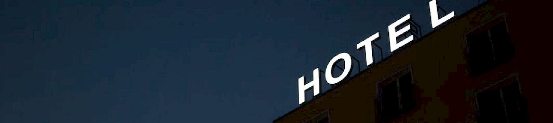A building with a glowing "HOTEL" sign on its top corner against a dark sky.