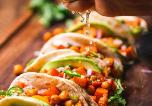 The image shows tacos filled with chickpeas, vegetables, and avocado, with a hand squeezing lime juice over them.