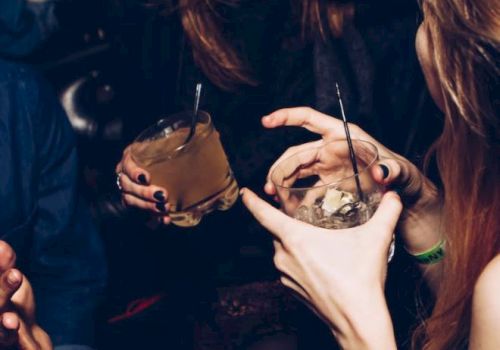 People are socializing and laughing, holding drinks with straws, in what appears to be a dimly lit setting.