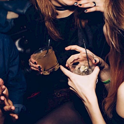 People are socializing and laughing, holding drinks with straws, in what appears to be a dimly lit setting.