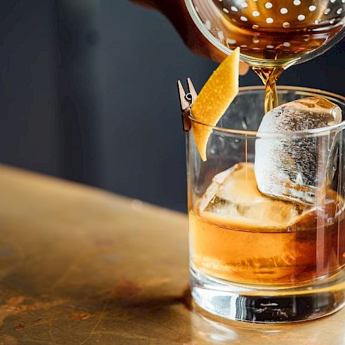 A cocktail is being poured into a glass with ice and a citrus twist garnish.
