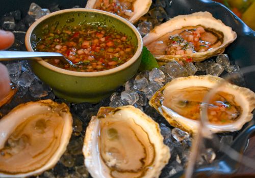 Fresh oysters on ice with a tangy dipping sauce in a green bowl, lemon wedges, and crusty sides, ready to share for a seaside feast.