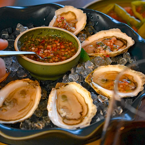 Fresh oysters on ice with a tangy dipping sauce in a green bowl, lemon wedges, and crusty sides, ready to share for a seaside feast.