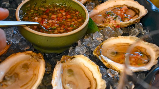 Fresh oysters on ice with a tangy dipping sauce in a green bowl, lemon wedges, and crusty sides, ready to share for a seaside feast.