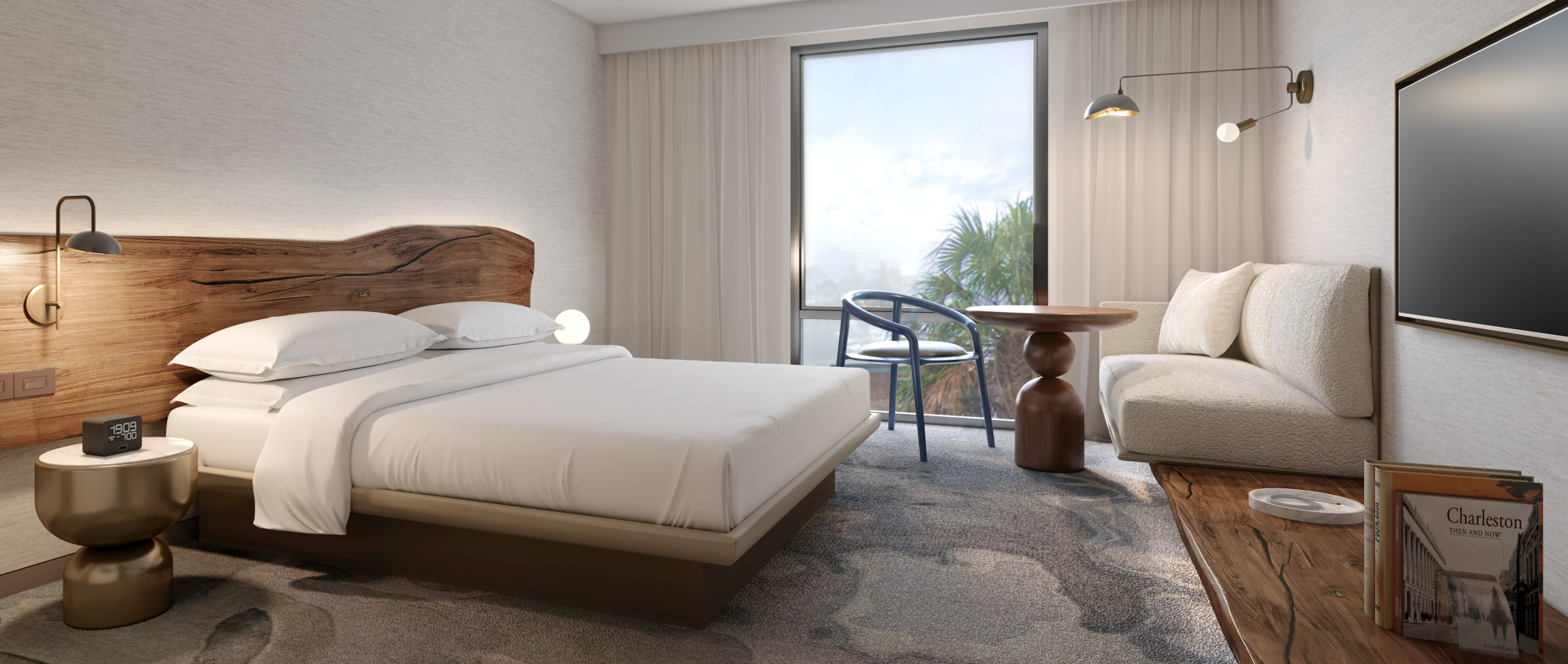 A modern hotel room with a large bed, a sofa, a small table with chairs, and a TV. A window reveals a scenic outdoor view.