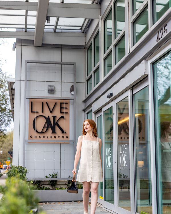 A stylish woman in a white dress stands outside a modern storefront with a wooden &ldquo;LIVE OAK&rdquo; sign, bright windows, and urban architecture.