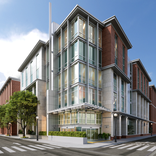 A modern building with glass windows and brick siding is on a corner with crosswalks and trees, under a clear blue sky.