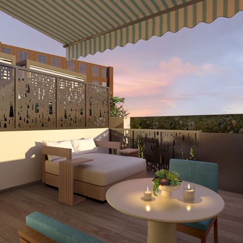 A cozy patio with a lounge chair, a table with candles, a striped awning, and decorative fencing, at sunset.