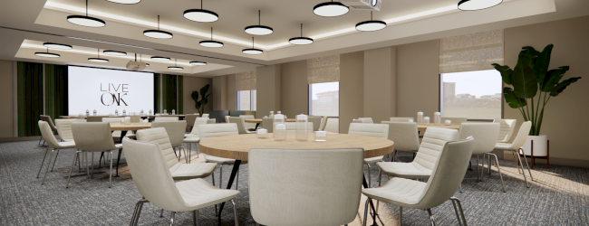 The image shows a modern conference room with round tables, chairs, plants, and a screen. Ceiling lights are evenly distributed.