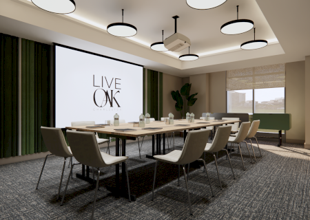A modern conference room with a long table, chairs, a screen displaying "LIVE OAK," and large windows for natural light.