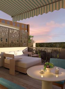 A cozy terrace with a lounge chair, table with candles, decorative railing, and striped awning under a sunset sky.