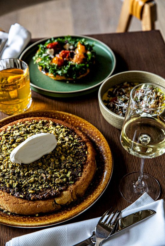 A cozy meal scene with a herb-crusted tart and greens, a salad, and a glass of white wine on a wooden table, inviting and stylish.