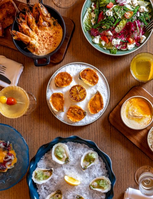 A top-down spread of assorted brunch dishes: dumplings, mini tarts, salad, bread bowls, roasted veggies, sauces, yogurt, and drinks. End.