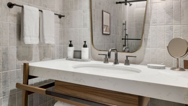 A modern bathroom sink area with a marble countertop, two black soap dispensers, a round mirror, and white towels.