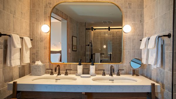 A double-sink bathroom with a large arched mirror, two sconces, and neatly arranged towels and toiletries on the counter, warm lighting.