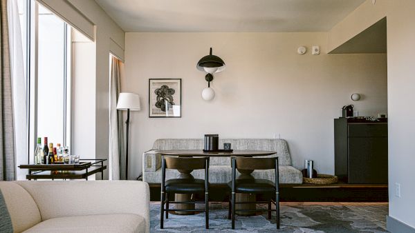 A stylish mid-century living room with a gray sofa, black dining table and chairs, a tall floor lamp, a wall art print, and a bar area by large windows, bright and airy.