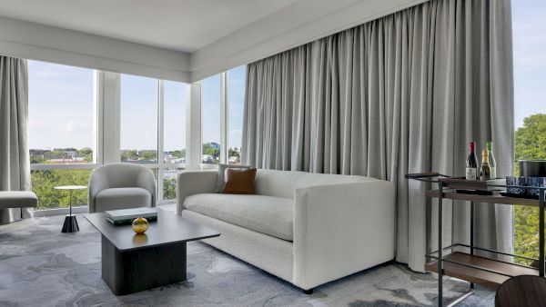 A bright, modern living room with a light sofa, large windows, gray curtains, a sleek coffee table, and a bar cart on the side.