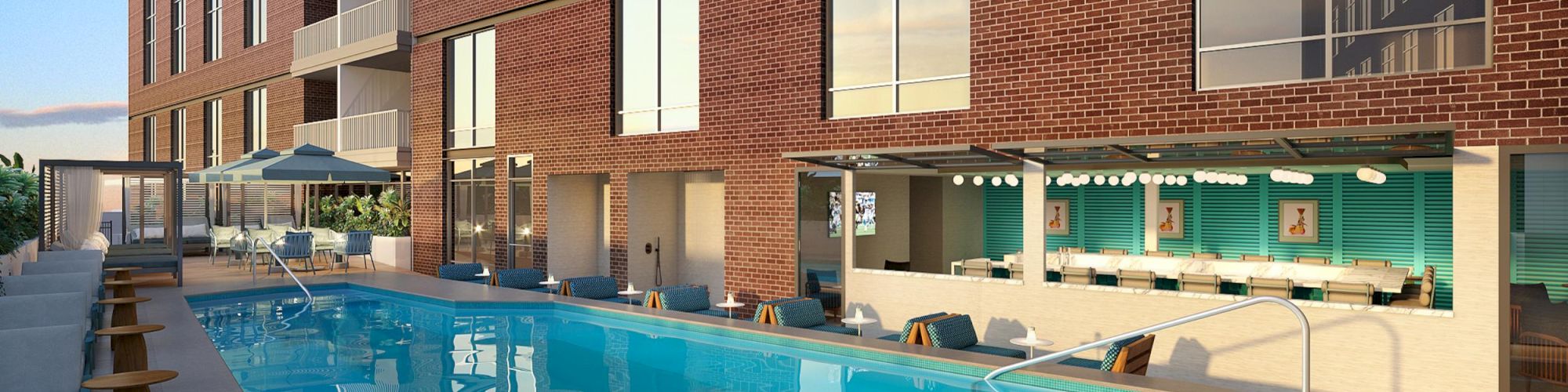 A modern outdoor pool area with lounge chairs, a brick building, and a bar area with stools and umbrellas nearby.