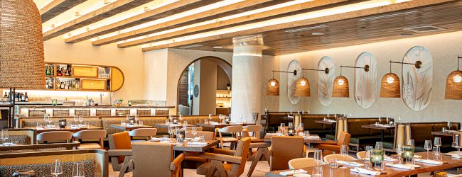 A stylish restaurant interior with warm lighting, wooden tables and chairs, arched wall niches, and a bar area in the background.