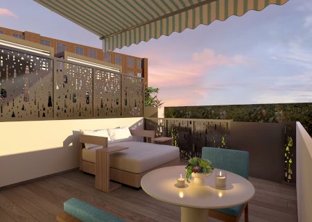 A cozy terrace with seating, a small table, candles, and decorative fencing under a striped awning at sunset.