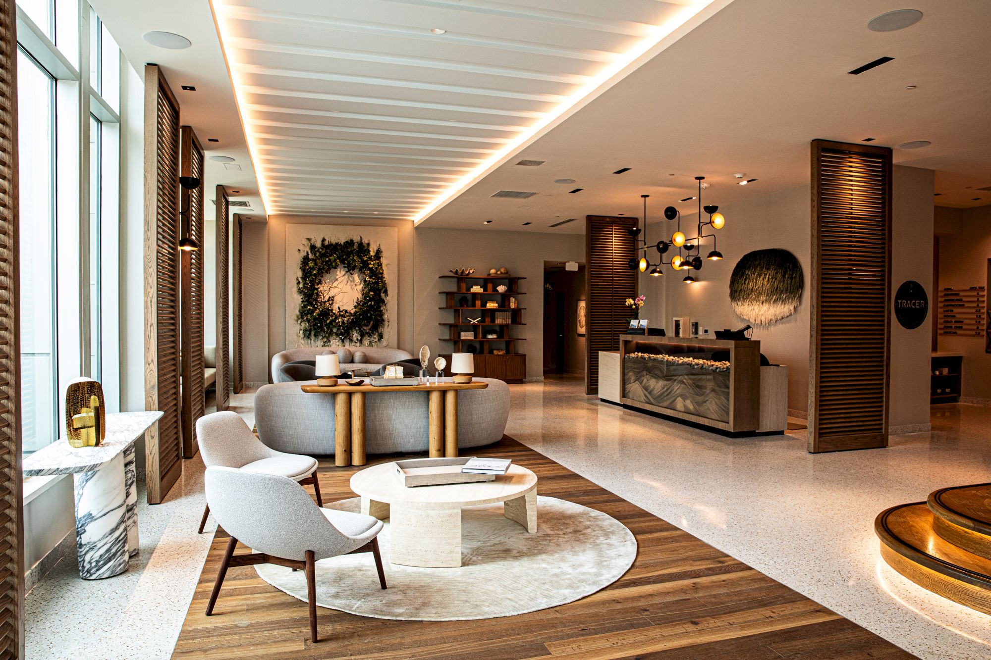 A chic hotel lobby with a circular seating area, soft gray chairs, wooden accents, a reception desk, and warm ambient lighting, welcoming and elegant.