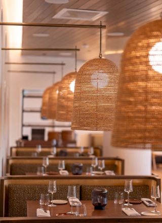 A stylish restaurant interior with woven pendant lights over booths, tables set with glassware and cutlery, a cozy dining vibe.