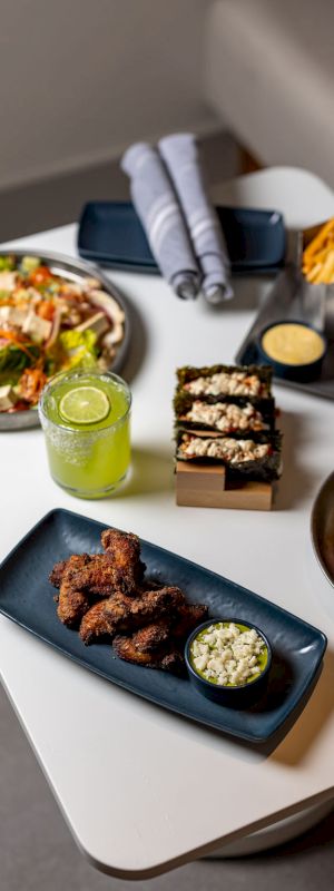 A table with various foods: a salad plate, sliders, fries, a green juice, a bowl of meat bites with dip, and a small dish of cookies.