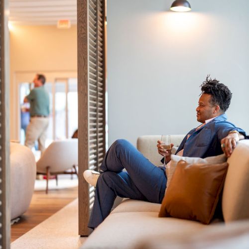 A cozy, sunlit living room with a man lounging on a light sofa, a small coffee table, plants, and warm vibes.