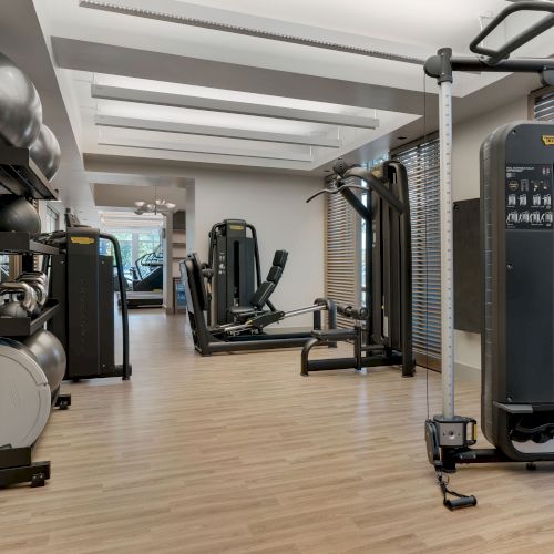Modern gym with TechnoGym machines, weight stacks, and padded workout stations under bright ceiling lights.