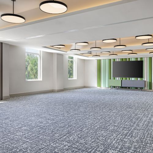 A modern conference room with gray carpet, large windows, a central screen, green-and-white wall panels, and round pendant lights.