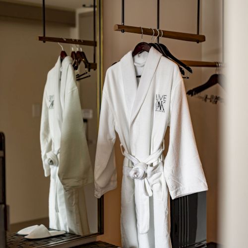 Two plush bathrobes hang on hooks in a cozy, wooden-wardrobe corner with a small bench and soft lighting.