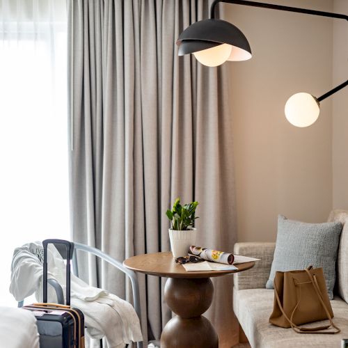 A cozy, well-lit living room with a pendant lamp, draped curtains, a wooden coffee table, a sofa with pillows, and a small plant on the table.