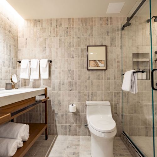 A compact hotel room with a single bed, desk, chair, wall art, and a tiled bathroom visible through a doorway, cozy and minimal.