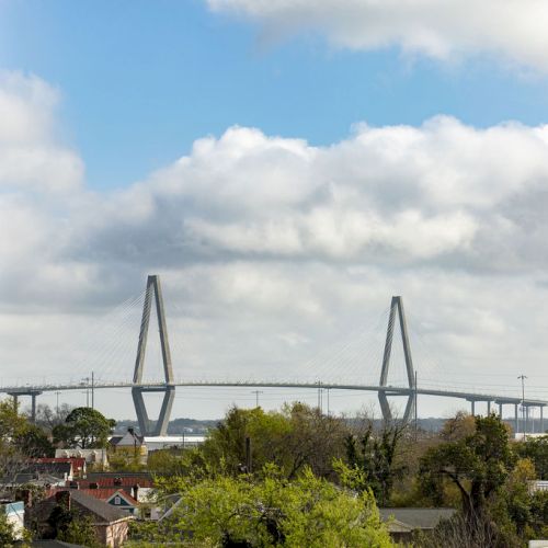 A cyclist rides along a narrow path by a canal with grassy banks and a cloudy sky, a scene of calm outdoor activity.
