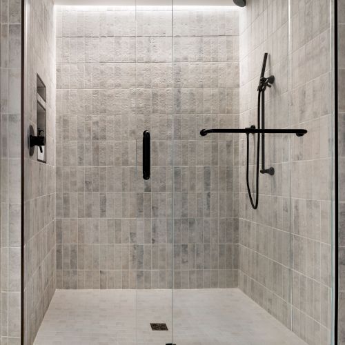 A tiled walk-in shower with glass doors and black rainfall/handheld fixtures, plus a floor drain in the enclosure.