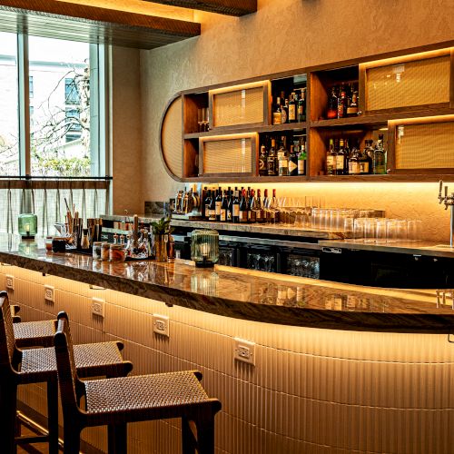 A cozy kitchen and dining area with warm wood tones, an island, bar stools, rustic shelves, and soft ambient lighting.