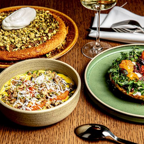 A colorful spread of Thai dishes: curries, noodles, and fresh greens, plus a dessert in a small bowl, all on a rustic wooden table.
