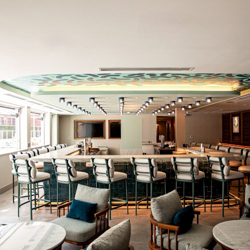 A stylish, circular bar or conference area with a long curved counter, high stools, and cozy lounge chairs around small tables, under soft lighting.