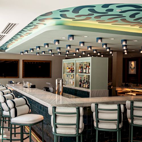 A casino table area with green felt, cards, chairs, and poker chips, dim lighting, and a backlit sign in a wood-trimmed room.