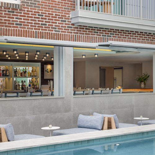Outdoor poolside lounge with brick walls and a built-in bar window stocked with bottles and warm lighting.