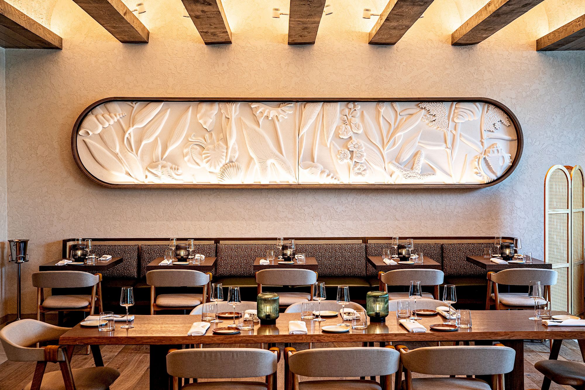 A stylish dining room with a long wooden table, modern chairs, candles, and a sculpted oval wall art piece; warm, intimate ambiance.