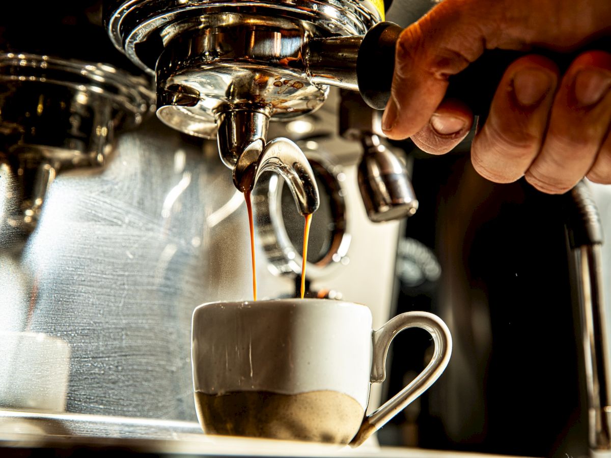 A close-up of an espresso machine pouring coffee into a white cup, steam rising as a barista taps the lever.