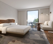 A bright hotel room with a king bed, wooden headboard, night lamps, a seating area, desk, and a large window with sheer curtains.