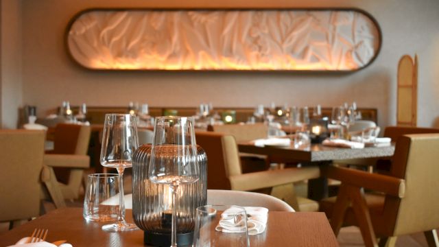 A stylish restaurant dining room with wooden tables, elegant glassware, soft lighting, and upholstered chairs, ready for guests.