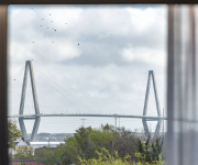 A large cable-stayed bridge spans a river under a cloudy sky, seen framed through a window.