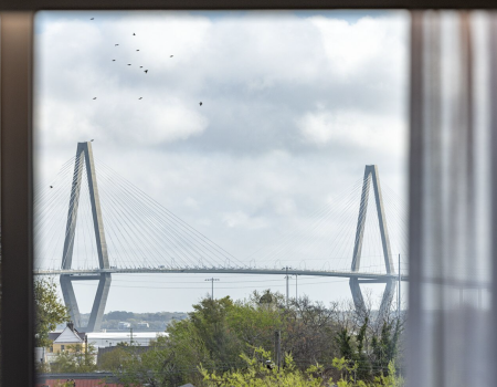 A large cable-stayed bridge spans a river under a cloudy sky, seen framed through a window.