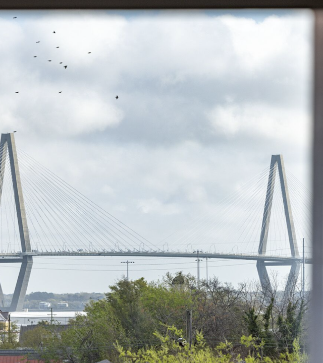 A large cable-stayed bridge spans a river under a cloudy sky, seen framed through a window.