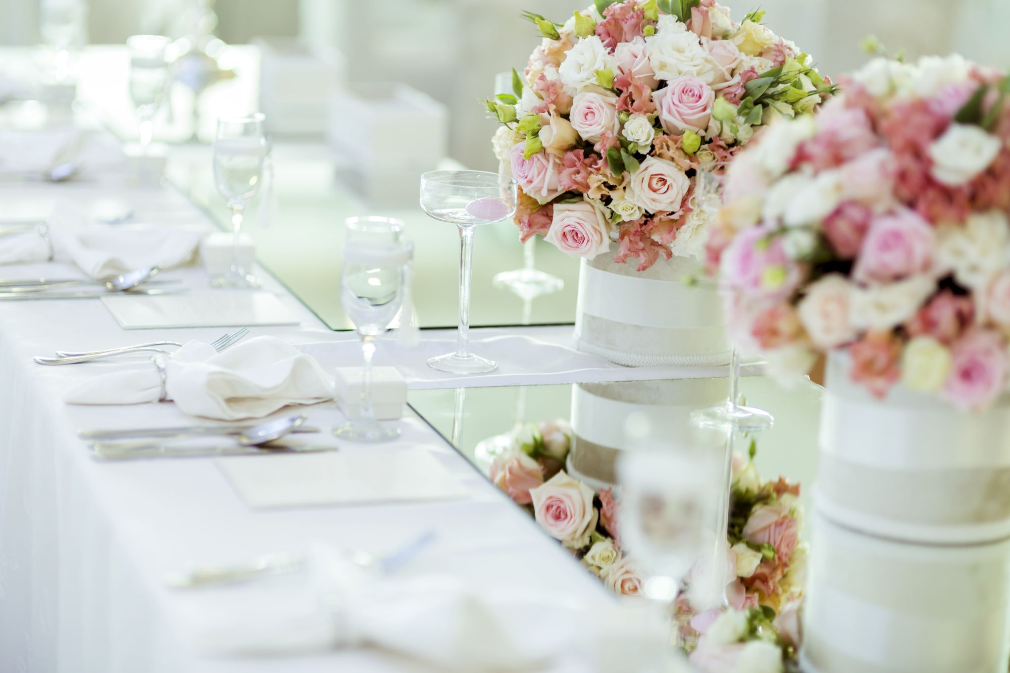 A bright table setting with wine glasses and a large pastel rose bouquet centerpiece for a wedding or celebration.