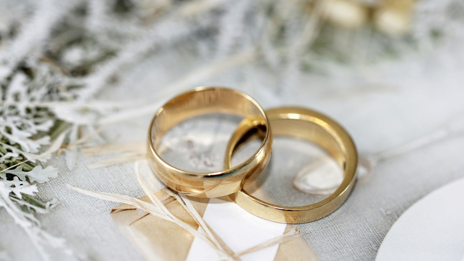 Two gold wedding rings resting on light fabric with soft-focus leaves in the background.
