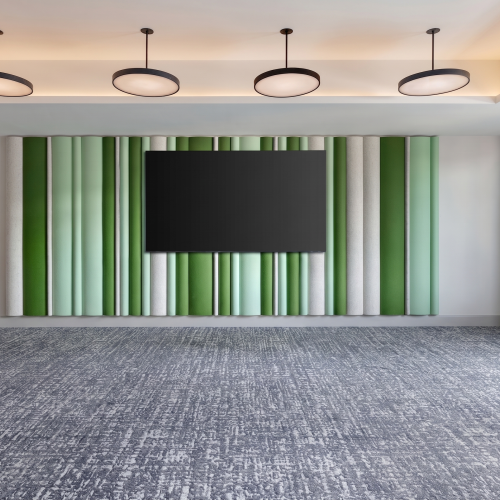 A modern meeting room with a large TV on striped green curtains, carpeted floor, and four hanging ceiling lights.